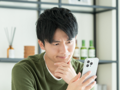 写真：スマホを見ながら悩んでいる男性