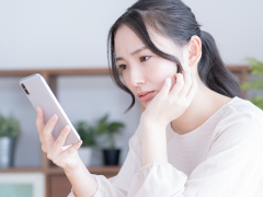 写真：スマホを見る困った表情の女性