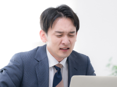 写真：職場でパソコンを前に困った表情のスーツの男性